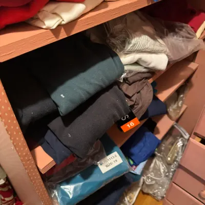 Sale Photo Thumbnail #147: Shelves stacked with various folded clothing items, including t-shirts and pants, in assorted colors and sizes.