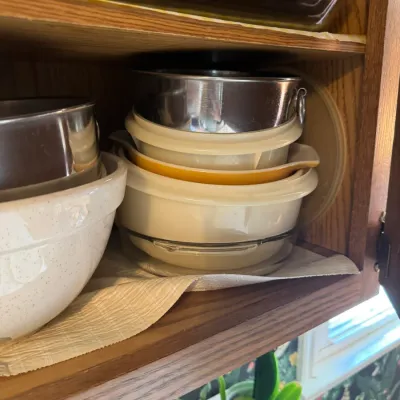 Sale Photo Thumbnail #256: Collection of vintage mixing bowls and baking dishes, including Pyrex cinderalla bowls and a speckled ceramic bowl, stacked inside a wooden cabinet.