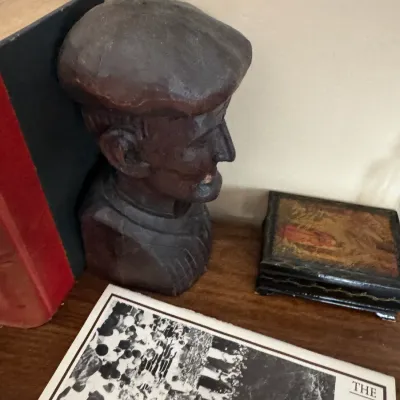 Sale Photo Thumbnail #314: Hand-carved wooden bust of a man in a cap, positioned as a bookend alongside a vintage lacquered trinket box and printed media.