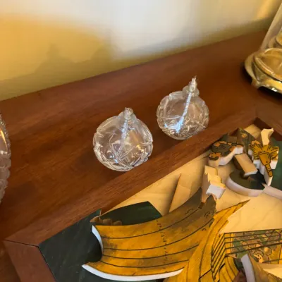Sale Photo Thumbnail #353: Pair of small spherical cut crystal oil lamps with wicks sitting on a wooden surface beside wooden puzzle pieces.
