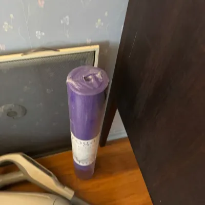 Sale Photo Thumbnail #175: Rolled purple yoga mat in factory plastic wrapping, shown alongside a framed mesh screen and part of a vacuum cleaner.