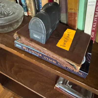 Sale Photo Thumbnail #311: Vintage cast metal treasure chest-style coin bank sitting atop stacked hardback books on a wooden bookshelf.