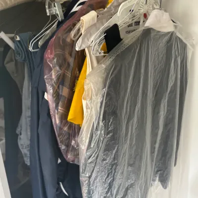 Sale Photo Thumbnail #130: Selection of vintage and modern clothing hanging in a closet, including jackets, denim, and dry-cleaned garments.