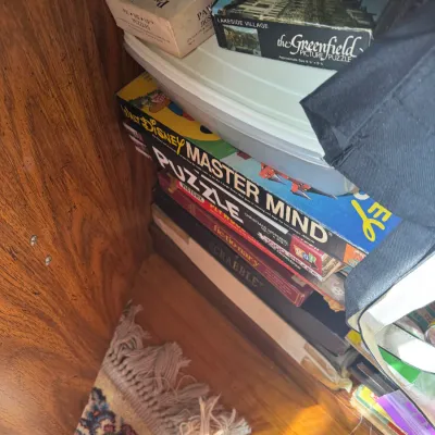 Sale Photo Thumbnail #295: Stack of vintage board games and jigsaw puzzles stored in a wooden cabinet, including Mastermind, Scrabble, and Greenfield Picture Puzzles.