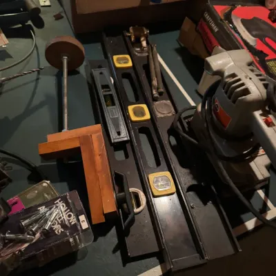 Sale Photo Thumbnail #89: Assortment of hand and power tools including multiple bubble levels, a wooden square, hollow wall anchors, and a vintage power sander.