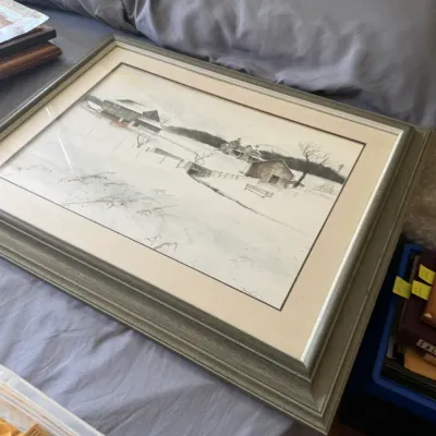 Sale Photo Thumbnail #124: Framed winter landscape watercolor print depicting a snowy farm scene, housed in a wide gray molding frame with double matting.