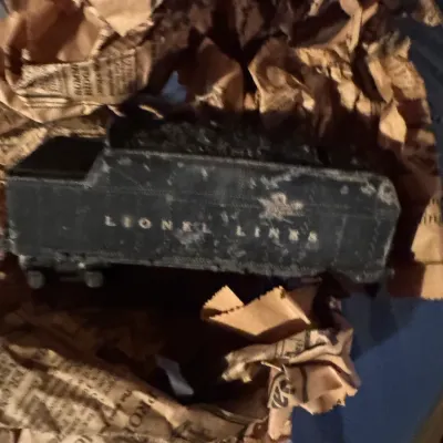 Sale Photo Thumbnail #82: Vintage Lionel Lines black coal tender car, unwrapped from old newspaper with visible wear and surface distress.