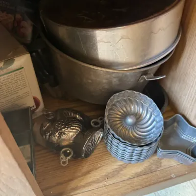 Sale Photo Thumbnail #223: Assorted vintage baking pans and molds stored inside a wooden cabinet, including cake pans, mini bundt tins, and a novelty turkey-shaped mold.
