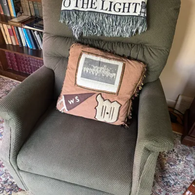 Sale Photo Thumbnail #281: Green fabric upholstered recliner chair featuring a custom memory pillow with a sports team photo and patch, topped with a woven graphic throw blanket.