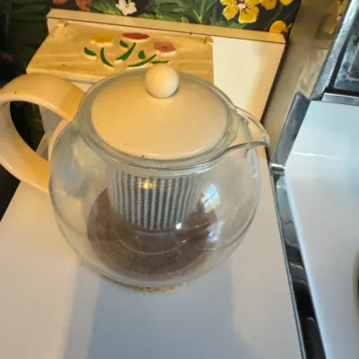 Sale Photo Thumbnail #271: Clear glass teapot featuring a cream-colored handle and lid with an interior infuser insert.