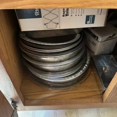 Sale Photo Thumbnail #226: Stack of assorted baking pans and pie tins stored inside a wooden cabinet alongside boxed kitchen accessories.