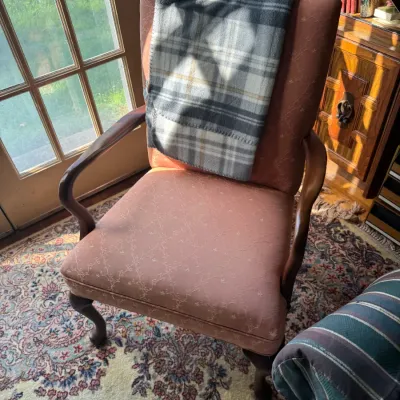 Sale Photo Thumbnail #302: Vintage Queen Anne style armchair with dusty rose embroidered upholstery and wooden cabriole legs, paired with a grey plaid throw blanket.