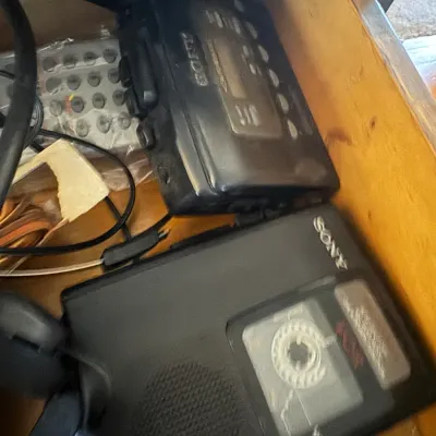 Sale Photo Thumbnail #178: Vintage Sony Walkman personal cassette players stored in a wooden drawer alongside headphones and remotes.