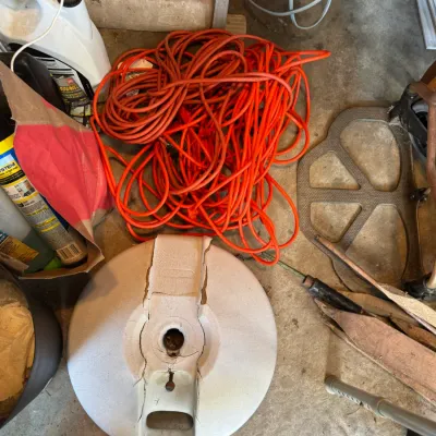 Sale Photo Thumbnail #197: Collection of garage items including a heavy-duty orange extension cord, a cracked plastic umbrella stand base, and lawn chemicals.