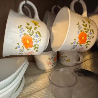 Sale Photo Thumbnail #32: Vintage Corelle or CorningWare teacups featuring a retro floral pattern, hanging under a cabinet shelf alongside matching dishes.