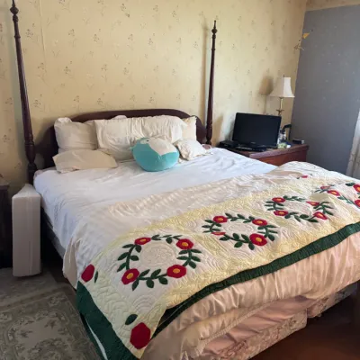 Sale Photo Thumbnail #188: Four-poster wooden bed dressed with white linens and a handmade floral quilt folded at the foot.