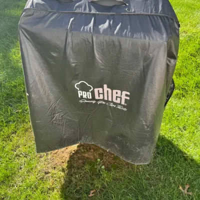 Sale Photo Thumbnail #209: Outdoor grill or appliance fully covered with a black Pro Chef protective cover, weighted down with two bricks on top.
