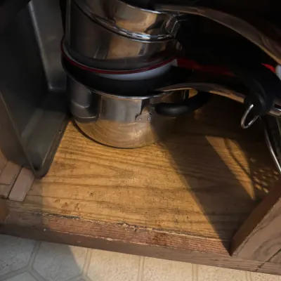 Sale Photo Thumbnail #250: Stack of stainless steel pots and a baking pan stored inside a wooden kitchen cabinet.