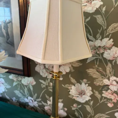 Sale Photo Thumbnail #385: Traditional brass column table lamp with a cream-colored fabric lampshade, set against floral wallpaper.