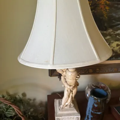 Sale Photo Thumbnail #357: Vintage classical-style table lamp featuring a cherub figure holding an urn, paired with an off-white fabric shade.
