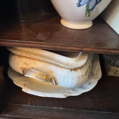 Sale Photo Thumbnail #379: Antique porcelain tureen with gilt accents resting on an undertray inside a wooden cabinet.