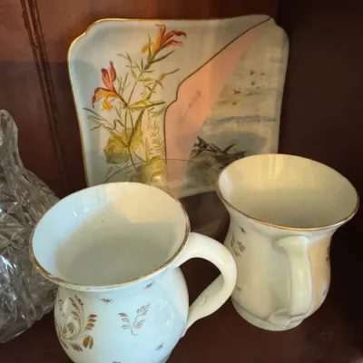 Sale Photo Thumbnail #403: Vintage porcelain mug set with gilt floral accents, displayed alongside a floral-painted porcelain tray and crystal glassware on a wooden shelf.