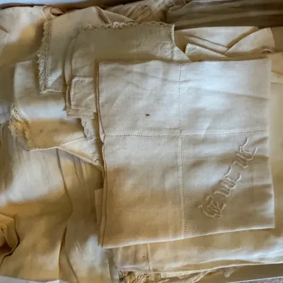 Sale Photo Thumbnail #334: Collection of vintage white and cream linens, featuring lace trim and embroidered monograms, folded inside a storage box.