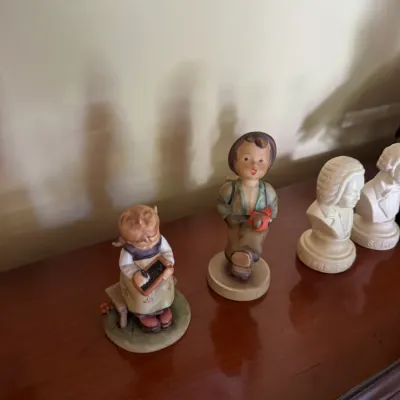 Sale Photo Thumbnail #325: Pair of vintage Goebel Hummel porcelain figurines displayed on a wooden surface alongside small white bust sculptures.