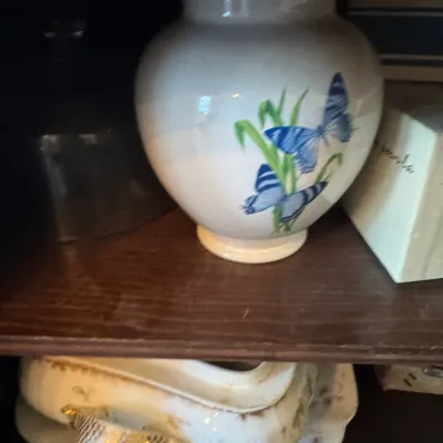 Sale Photo Thumbnail #378: White ceramic vase painted with blue butterflies and greenery, sitting on a wooden shelf alongside an antique porcelain tureen and undertray.