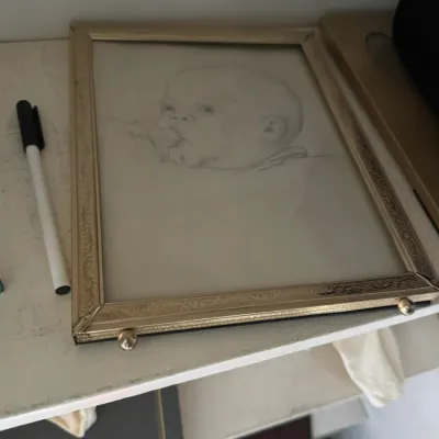 Sale Photo Thumbnail #127: Framed vintage pencil sketch portrait of a baby in an ornate gold-tone metal frame with ball feet.