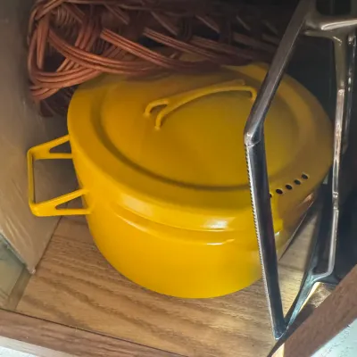 Sale Photo Thumbnail #28: Bright yellow enameled covered Dutch oven stored in a cabinet alongside a wicker basket and metal stand.