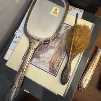 Sale Photo Thumbnail #168: Vintage tarnished silver-plated vanity set featuring a bevel-edged hand mirror, matching hairbrush, and associated vanity accessories.