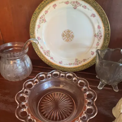 Sale Photo Thumbnail #401: Vintage glass and china collection featuring an open lace pink depression glass bowl, a gold and green rimmed porcelain floral plate, and clear pressed glass serving pieces.