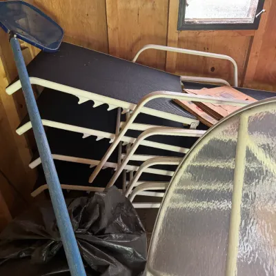 Sale Photo Thumbnail #68: A stack of outdoor patio loungers with white metal frames and dark mesh fabric, accompanied by a pool skimmer net and a glass-top patio table frame.