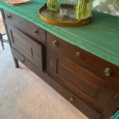 Sale Photo Thumbnail #377: Antique wooden buffet or sideboard featuring brass hardware, panel doors, and upper and lower drawers, topped with a green cloth runner.