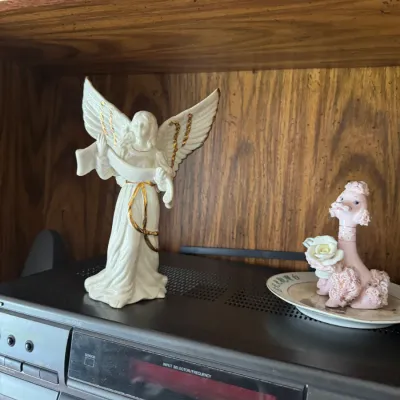 Sale Photo Thumbnail #306: White porcelain angel figurine with gold accents sitting alongside a vintage pink spaghetti-poodle figurine on top of an audio receiver.