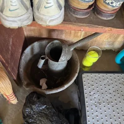 Sale Photo Thumbnail #192: Vintage flexible-spout galvanized oil can in an oil drain pan, stored on a floor with footwear and household items.