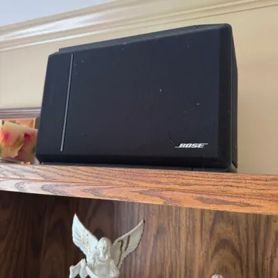Sale Photo Thumbnail #307: Black Bose bookshelf speaker sitting atop an oak cabinet, shown alongside decorative porcelain figurines.