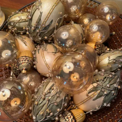 Sale Photo Thumbnail #51: A collection of gold and amber-toned Christmas tree ornaments, including clear glass spheres, beaded floral egg-shaped pieces, and acorn-styled drops displayed in a metal mesh bowl.