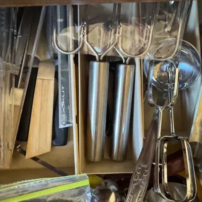 Sale Photo Thumbnail #253: Assorted stainless steel kitchen utensils including knives, ice cream scoops, and specialty servers stored in a wooden drawer organizer.