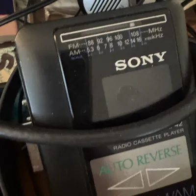 Sale Photo Thumbnail #179: Vintage black Sony Walkman portable AM/FM radio cassette player with auto reverse functionality and matching headphones.