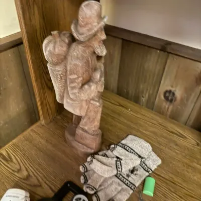 Sale Photo Thumbnail #95: Carved wooden figure depicting a bearded man with a pack, alongside a pair of patterned knit gloves and electronic accessories on a wooden shelf.