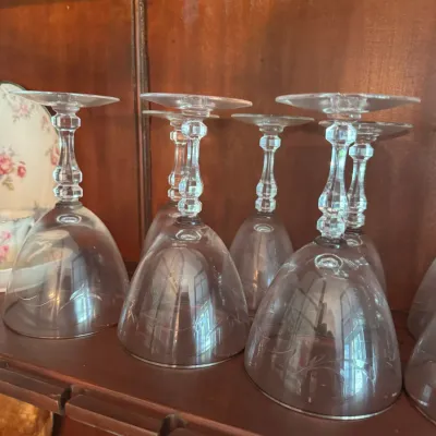Sale Photo Thumbnail #398: Set of vintage clear crystal stemware with etched floral details and multi-faceted stems, displayed upside down in a wooden cabinet.
