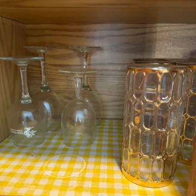 Sale Photo Thumbnail #243: Collection of glassware stored in a wooden cabinet, including Tree House Brewing wine glasses and mid-century modern gold honeycomb tumblers.