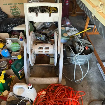 Sale Photo Thumbnail #196: Mobile molded plastic garden hose reel cart alongside a tangled orange extension cord and assorted workshop supplies.
