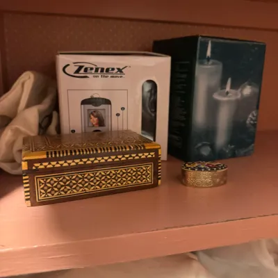 Sale Photo Thumbnail #148: Inlaid wooden trinket box displayed on a shelf alongside a small micro-mosaic pillbox and boxed household items.