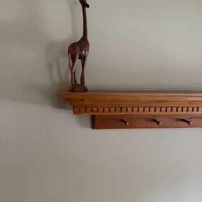 Sale Photo Thumbnail #109: Hand-carved wooden giraffe figurine displayed on a wooden wall-mounted coat rack shelf.