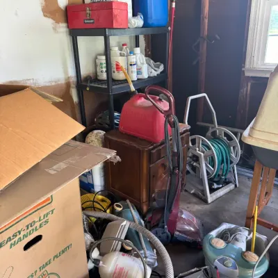 Sale Photo Thumbnail #194: Assorted workshop and household items including a hose reel cart, carpet cleaner, vacuum cleaner parts, foot spa, plastic gas can, and a black plastic shelving unit filled with chemicals.