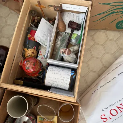 Sale Photo Thumbnail #216: Wooden crate filled with vintage knick-knacks and collectibles, including a stylized wooden cat, small gavel, nesting dolls, and figurines.