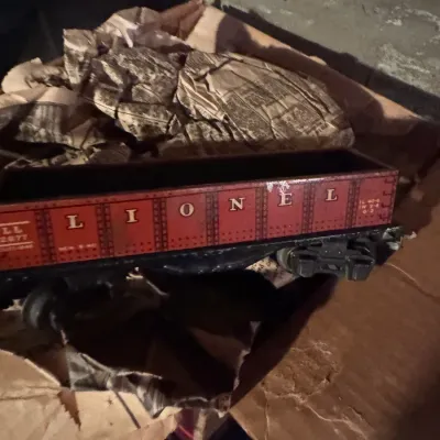 Sale Photo Thumbnail #81: Vintage Lionel red lithographed tinplate gondola train car, resting inside a cardboard box with newsprint packing material.